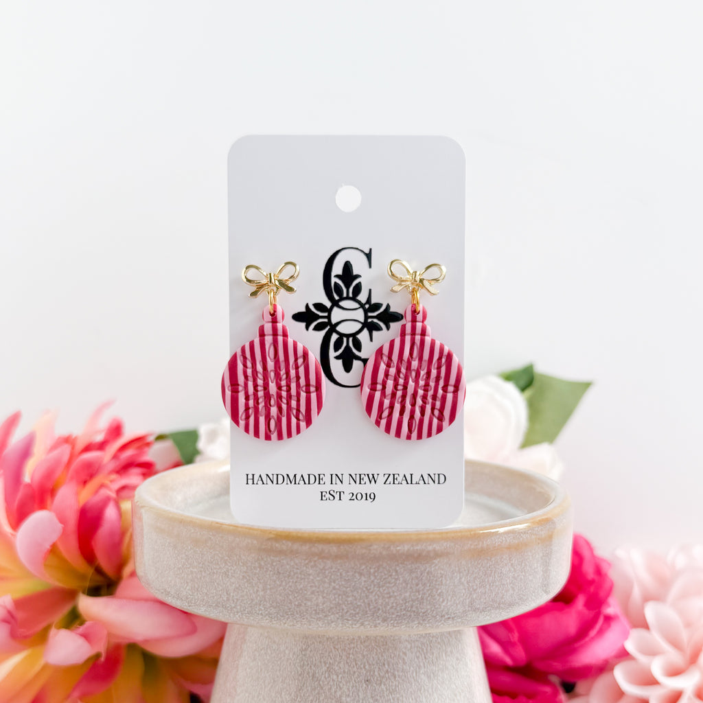 Pair of red earrings on a white card with branding, displayed against a floral background.